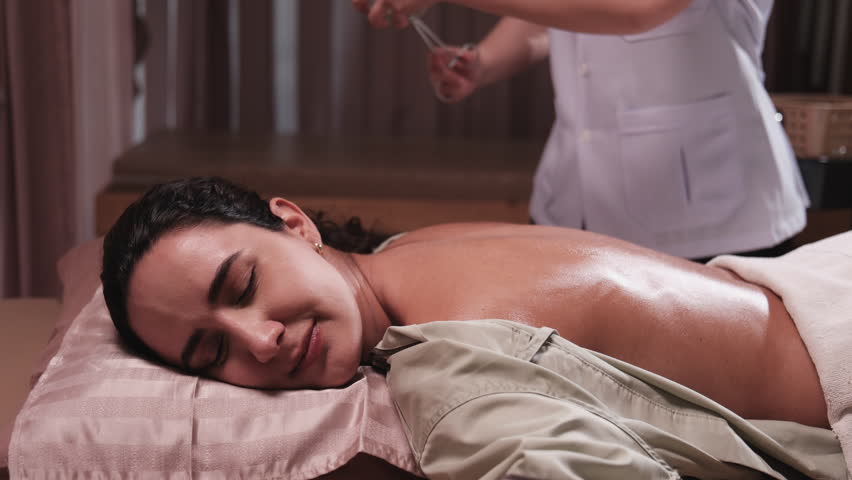 Beauty Latino woman is treated for healthy recovery with cupping therapy by Asian physical muscle doctor, an oriental traditional medicine therapist at a spa clinic, and wellness massaging lifestyle.