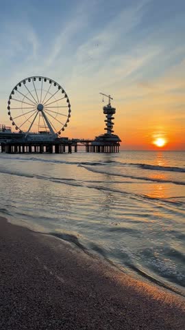Vertical video of a sunset on the beach in The Hague, Netherlands. The North Sea coast, Scheveningen Pier and the famous Ferris wheel, SkyView de Pier.