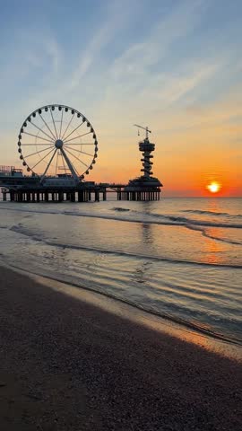 Vertical video of a sunset on the beach in The Hague, Netherlands. The North Sea coast, Scheveningen Pier and the famous Ferris wheel, SkyView de Pier.