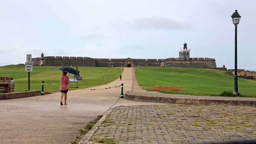 A woman with an umbrella walks towards El Morro