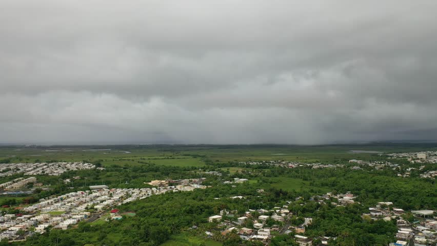 An aerial view of El Yunque National Forest landscape with scattered settlements and a freeway under gray clouds cover in Puerto Rico