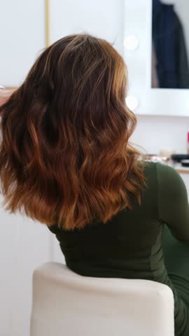 woman with medium length wavy brown hair sits in beauty salon chair during styling session, elegant and relaxed atmosphere, haircare, salon services, beauty business