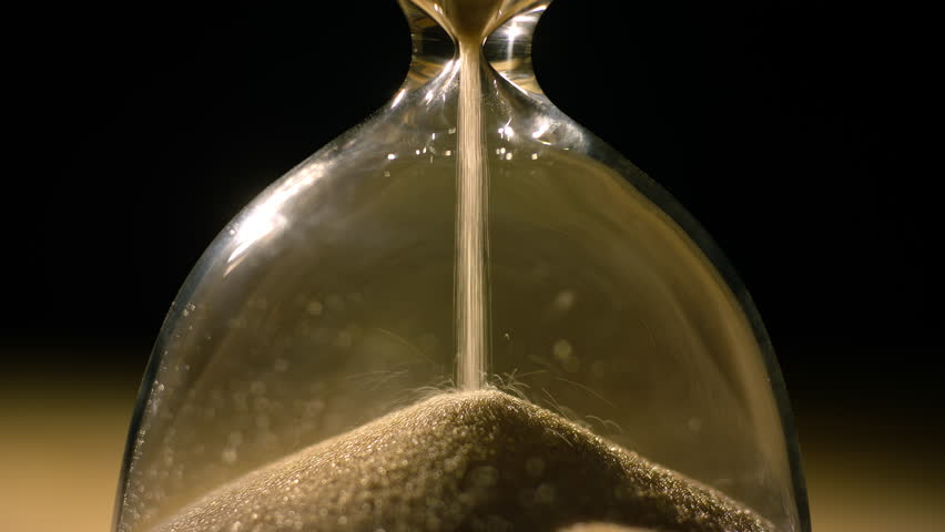 Golden sand leaking through the hourglass, measuring the passage of time, extreme close up shot. Deadline, moment, and evanescence concepts.