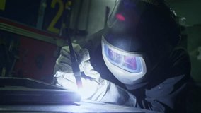 Focused and precise welder in protective workwear, face shield, and safety gloves, using a TIG welding machine in a dark workshop, close up shot. - Powered by Shutterstock - Get 15% off with code: PIKWIZARD15