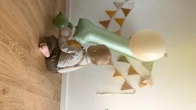 Cute baby boy celebrates 1 year birthday. Toddler plays on the floor among balloons and sage green inflatable number one. Child in beautiful costume and festive decor, vertical video. - Powered by Shutterstock - Get 15% off with code: PIKWIZARD15