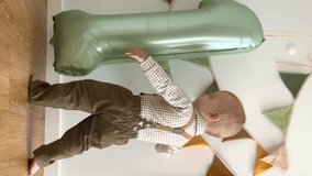Cute birthday baby boy with foil number one, vertical video. Toddler plays on the floor among balloons. Child in beautiful costume and festive decor.  - Powered by Shutterstock - Get 15% off with code: PIKWIZARD15