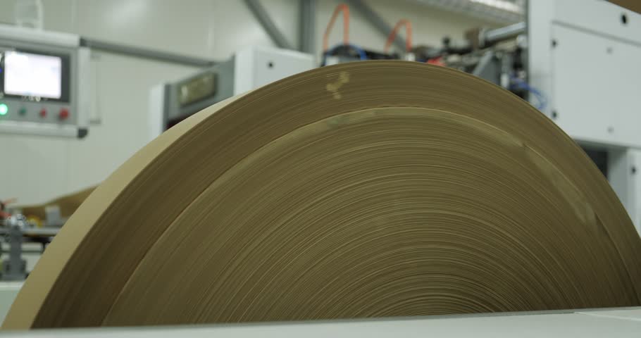 A large roll of paper is spinning on an industrial printing machine, a production process in a modern factory.
