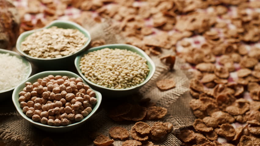 Close-up of carbohydrate-rich foods on a table, including bread, rice, wholegrain flakes, oats, wheat and corn pasta. Carbs Food.