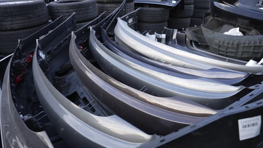Used car bumpers stacked at a car scrapyard, used car parts for recycling or resale.