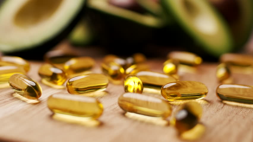 Avocado Oil Capsules with Avocado Halves in Background
