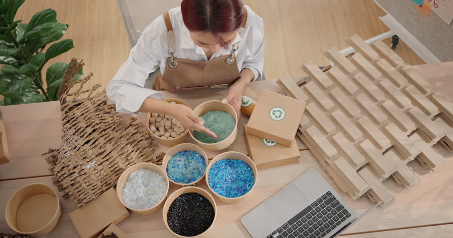 Top Down View, Go green Startup small business SME woman designer in apron with laptops picking sample of sustainable material reusable product in office. Eco-Friendly, environmental impact and waste