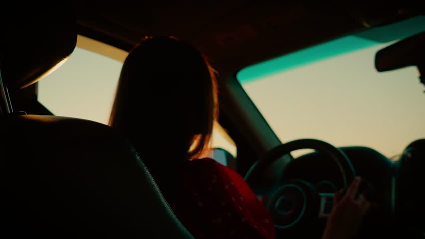 Cinematic shot woman driving car during sunset with dramatic lighting. Silhouette highlighted by warm golden hues as she holds steering wheel. Capturing serene mood of evening drive with focus on