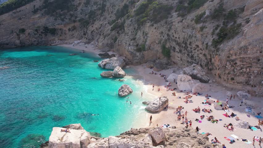 Aerial drone view on white sand Cala Baunei in Orosei Gulf of Sardegna. Warm turquoise sea and small beach surrounded with green mountains on the Sardinia island.
