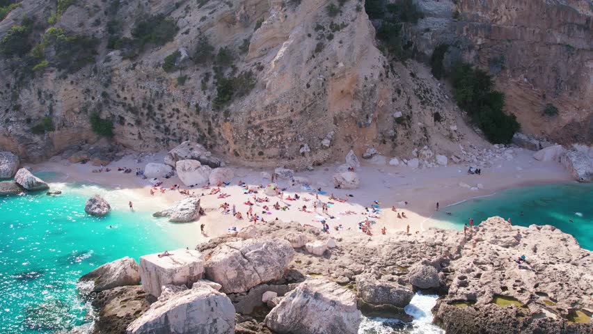 Aerial drone view on white sand Cala Baunei in Orosei Gulf of Sardegna. Warm turquoise sea and small beach surrounded with green mountains on the Sardinia island.