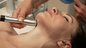 Performing Microcurrent Therapy on chin area of client. Device applying Ultrasound Facial Massage on lower face. Professional using Darsonval Treatment for skin tightening on jawline. Beautician - Powered by Shutterstock - Get 15% off with code: PIKWIZARD15