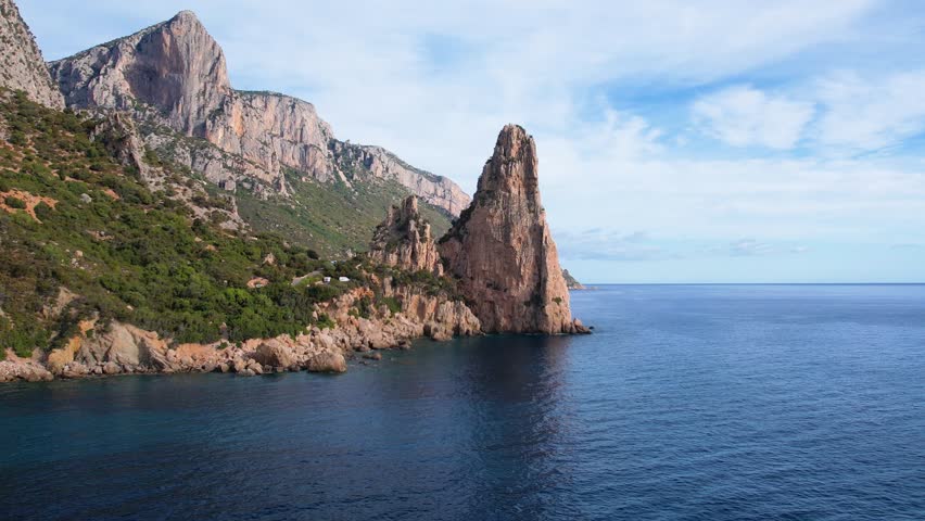 Aerial drone view of cliffs of Punrta Pedra Longa on Sardegna. Warm turquoise sea, height rocks and beach with green mountains on the Sardinia island.
