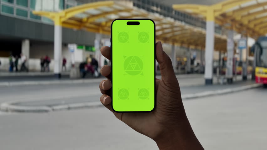 GREEN SCREEN CHROMA KEY Hand holding smartphone with green screen at a bus station, ideal for app or map mockups in urban transit settings
