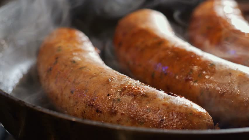 A detailed closeup of sausages getting cooked in a pan with rising smoke