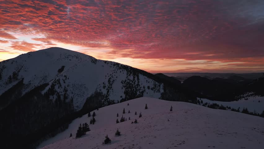 Bloody twilight sky glowing above snowy Alpine mountains at winter sunset, aerial view