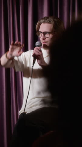 Vertical shot of young man in glasses telling funny story and joking during his stand-up performance on stage