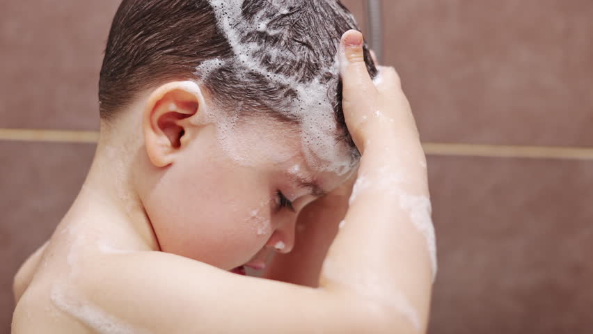 baby boy in bathroom shampooing hair and playing with water.close up kid feet.child taking liquid soap from dispenser.top view of smiling child lying in bathtub.shampoo bottle next to shower cabin.