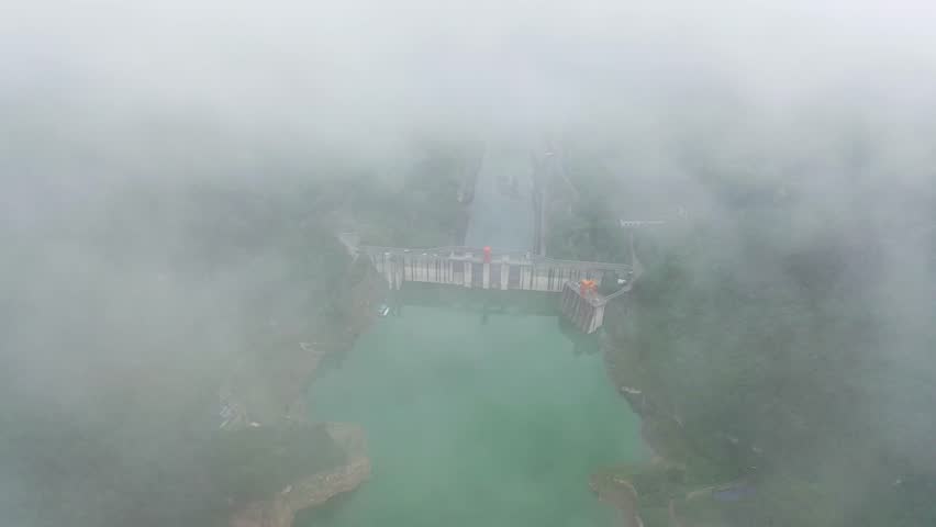 Spectacular aerial view of a dam surrounded by clouds over a serene lake in the early morning mist