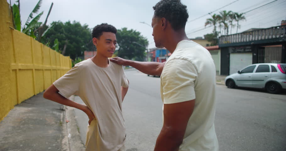 Father of African descent talking to son in an urban street, offering advice and encouragement with a reassuring gesture, emphasizing connection, mentoring, and family bond
