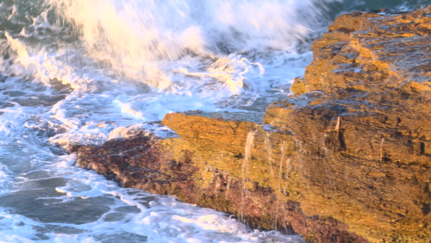 Close-up of a crashing wave hitting a rocky coast at sunset. Water splashes with dramatic force and golden light reflections in a breathtaking coastal seascape.