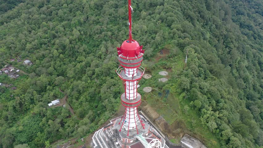 Aerial drone footage of the Turyapada Tower, a tall and iconic communications tower located in the mountains of northern Bali, Indonesia. Surrounded by mist and clouds, the tower stands majestically