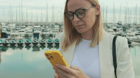 Professional businesswoman networking on yellow-cased smartphone near docked boats in nautical marina environment.Business, technology, blogging, communication concept - Powered by Shutterstock - Get 15% off with code: PIKWIZARD15