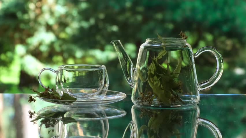 Linden Tea Pouring from Teapot into Glass Cup. Tea ceremony outdoors in summer or spring day. Refreshing Linden Herbal Tea in a Glass Cup
