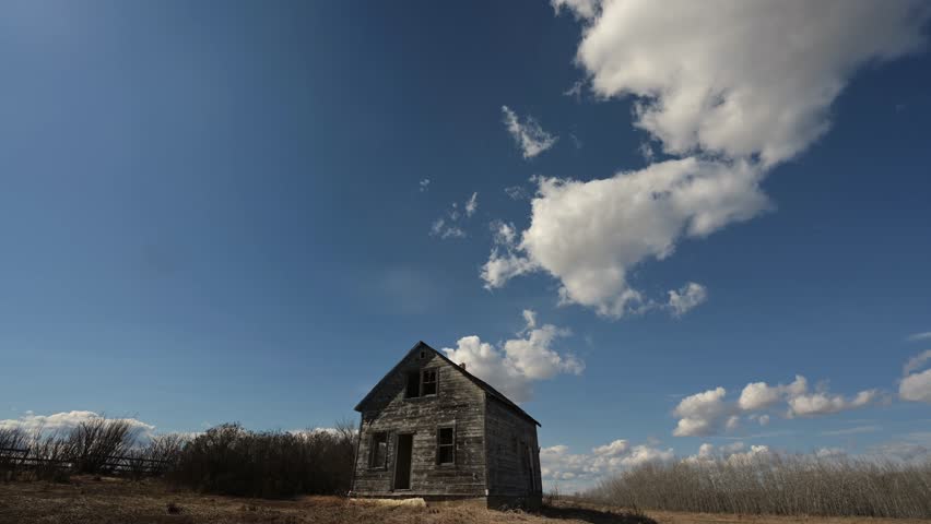 Time lapse of churning summer clouds in blue sky above an abandoned farmhouse

