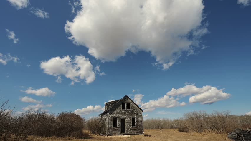 Time lapse of churning summer clouds in blue sky above an abandoned farmhouse
