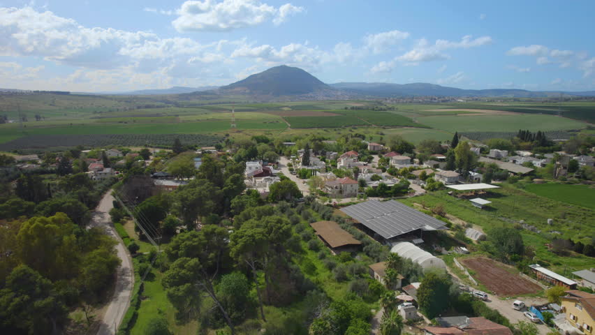 Mount Tabor creates a dramatic backdrop to this overhead shot of Kfar Kish - Israel, peaceful coexistence of village architecture with surrounding farmlands on a summer day in northern contry