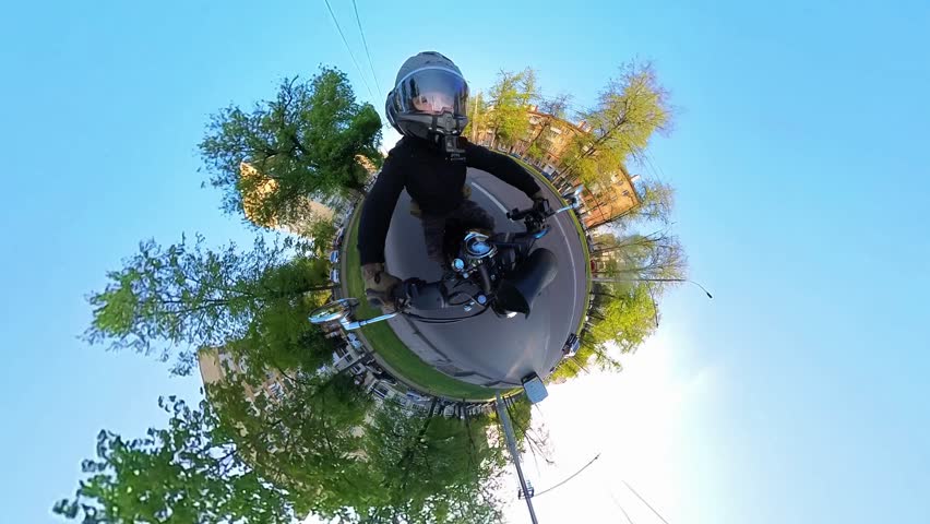 Circular 'little planet' distortion effect as a biker rides through city streets, casually resting hand on knee. Buildings and trees warp around handlebar-mounted camera