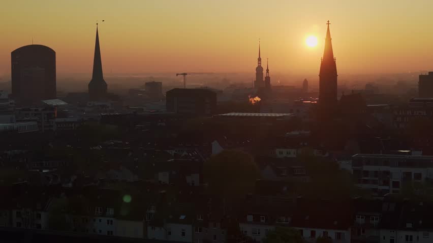 Dortmund City skyline silhouette with orange sunrise, bird flys across static telephoto drone shot