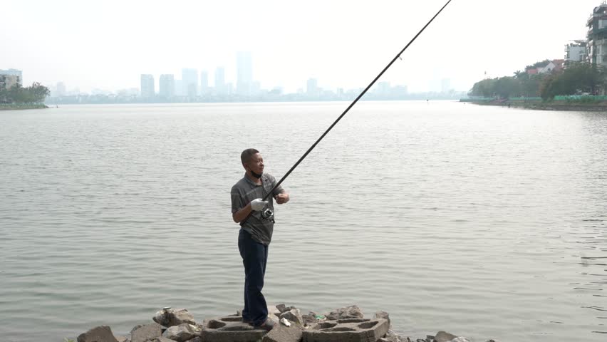 Casting fishing Asian man solitude, riverbank scenery, urban skyline