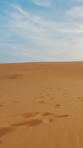 Couple runnin across desert golden sand dunes, leaving footprints behind, vertical video