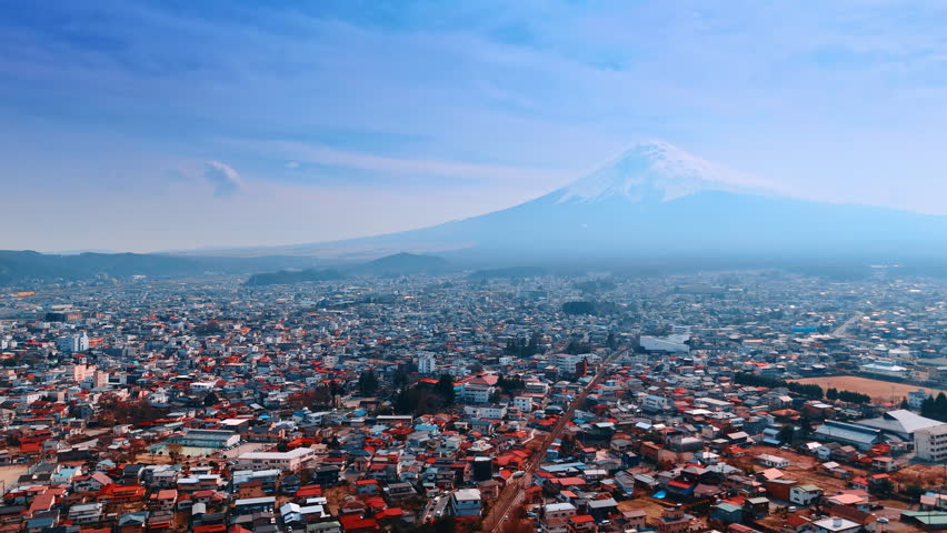 Vast sunny cityscape scattered at the foot of the hazy Mount Fuji, Honshu, Japan. Aerial perspective on the urban territory near stratovolcano.