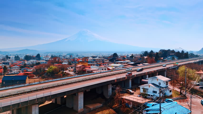 Cars go by the freeway crossing the cityscape of Tokyo. Magnificent Mount Fuji in the haze at backdrop. Aerial view.