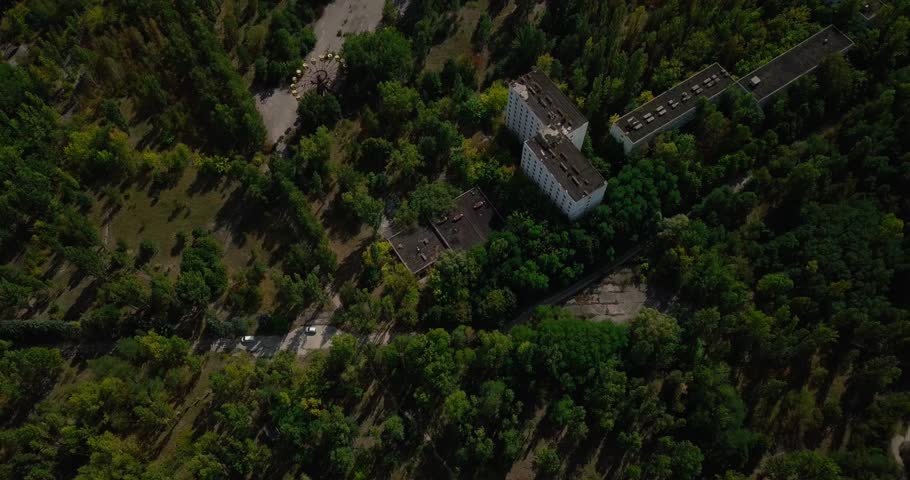 Cinematic top-down drone shot over Chernobyl’s abandoned buildings, now surrounded by dense forest. A haunting glimpse into the USSR’s past and nature reclaiming a lost city.