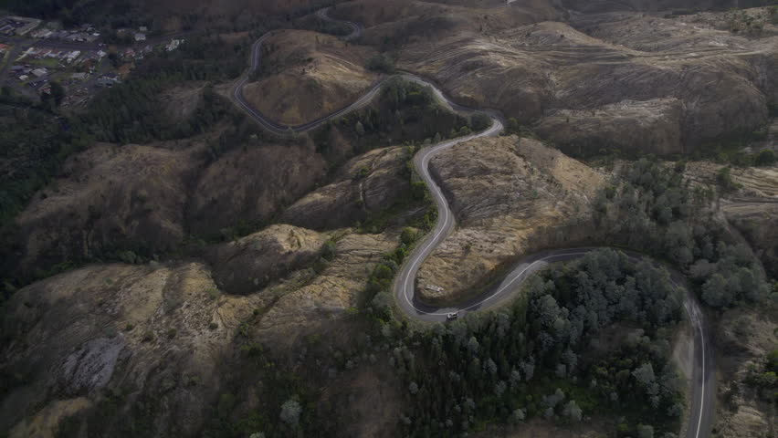Aerial drone shot of a van winding down the iconic 99 Bends near Queenstown, Tasmania. Surrounded by rugged brown hills, the road snakes through a dramatic and remote mountain landscape.