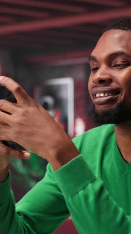 Vertical Video Man at home using smartphone to compose social media posts, producing content as a freelancer. African american guy monitoring profile engagement using mobile phone. Camera A.