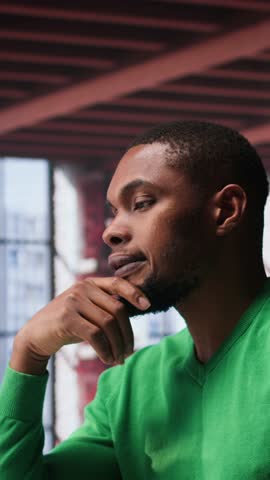 Vertical Video Black teleworker being pensive thinking about solutions to make more money, using his creativity and innovation for development. Young adult looking for new smart ideas. Camera B.