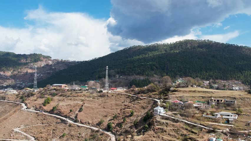 Wide aerial view of a hillside village near Murree with forested slopes and scattered homes