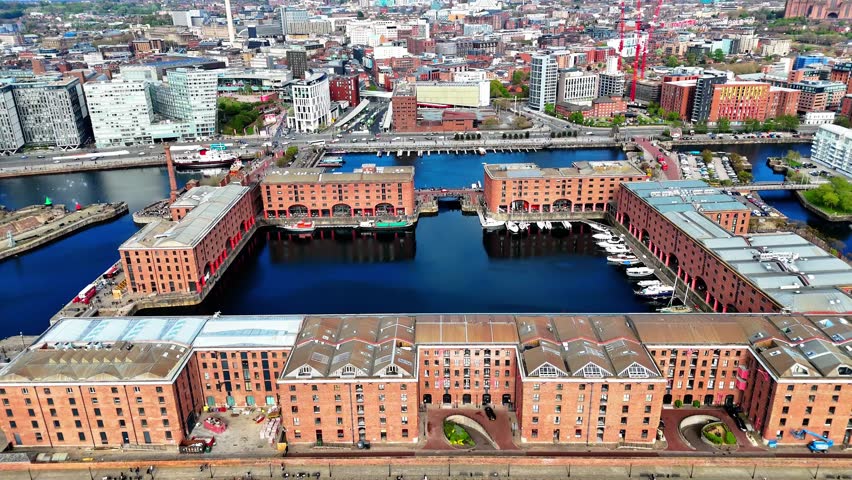 An aerial drone view pulls back from Liverpool's historic Dock, revealing the brick warehouses, marina, waterfront and city skyline.