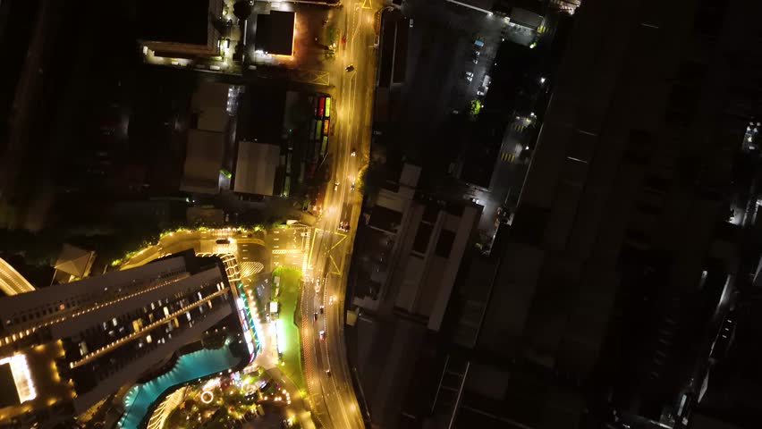 A top-down drone shot of nighttime traffic flowing through Kuala Lumpur, Malaysia, moving vehicles and illuminated roadways.