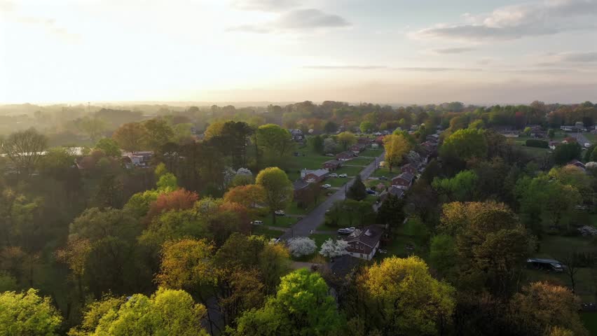 Aerial establishing shot of serene Atmosphere in american neighborhood. Golden sunrise rays in spring season. Wide shot. Two-story single Family houses wit green garden.