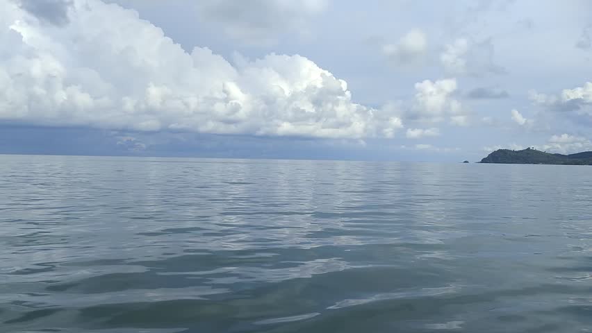 A peaceful seascape showcasing calm ocean waters with a distant headland and dramatic cloudy sky. Ideal for travel themes, backgrounds, or nature-related visuals emphasizing serenity and natural beaut