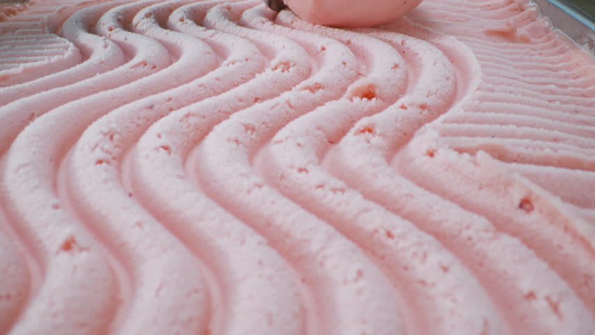 A close-up of a pink lemonade or strawberry ice cream being scooped out with a scoop. Smooth texture, vibrant color, and refreshing appearance.